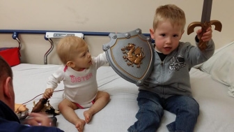 Brother with shield/sword, next to sister on hospital bed